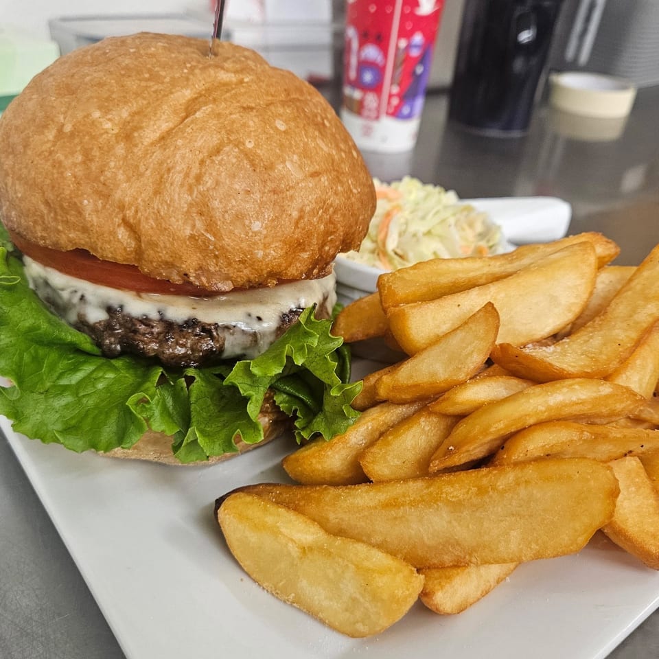 A cheeseburger with lettuce and tomato, served with wedge fries and coleslaw on a white plate.