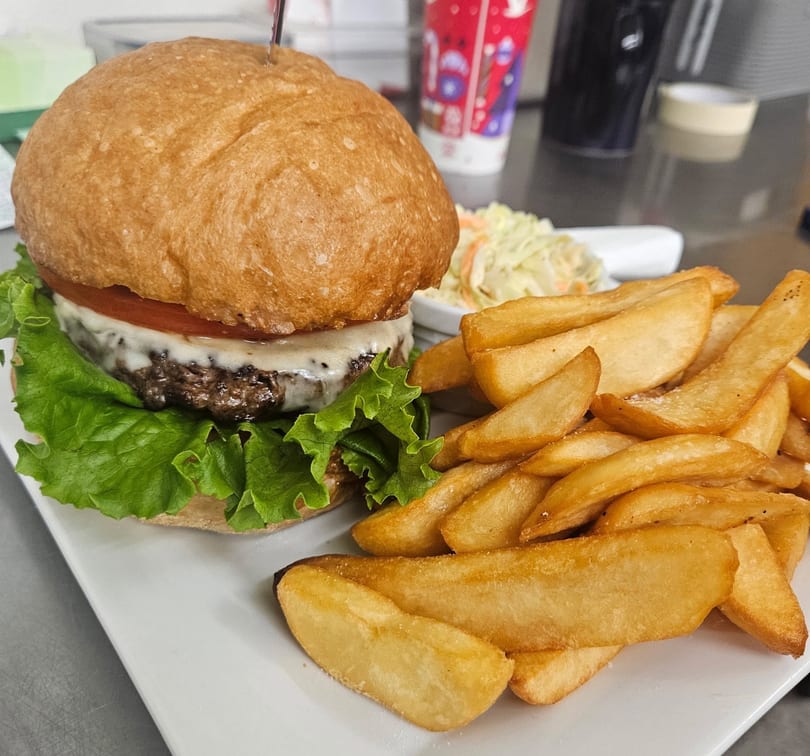 A cheeseburger with lettuce and tomato, served with wedge fries and coleslaw on a white plate.