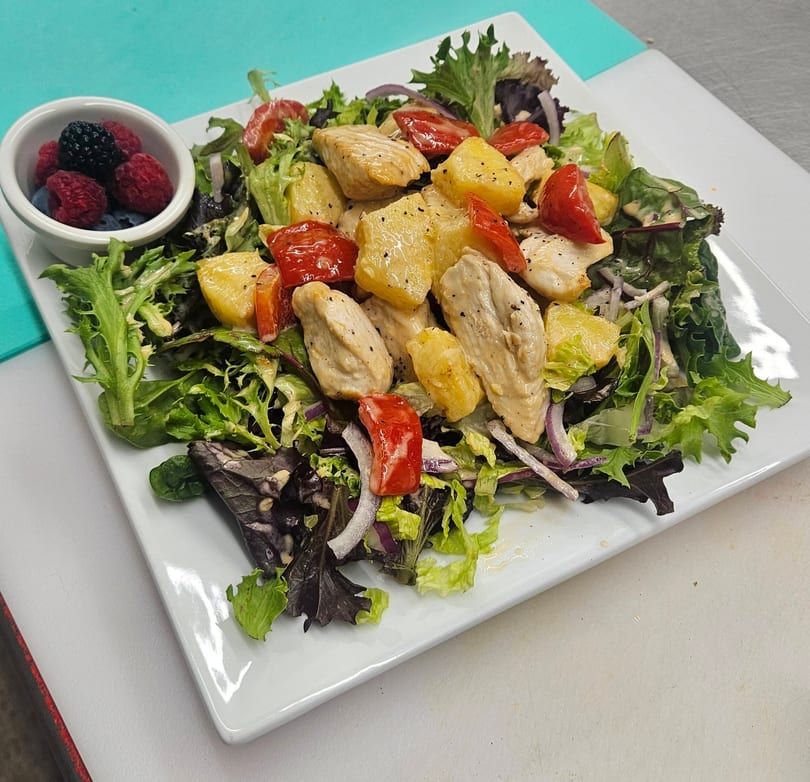Chicken and pineapple salad with mixed greens, tomatoes, and a side of fresh berries.